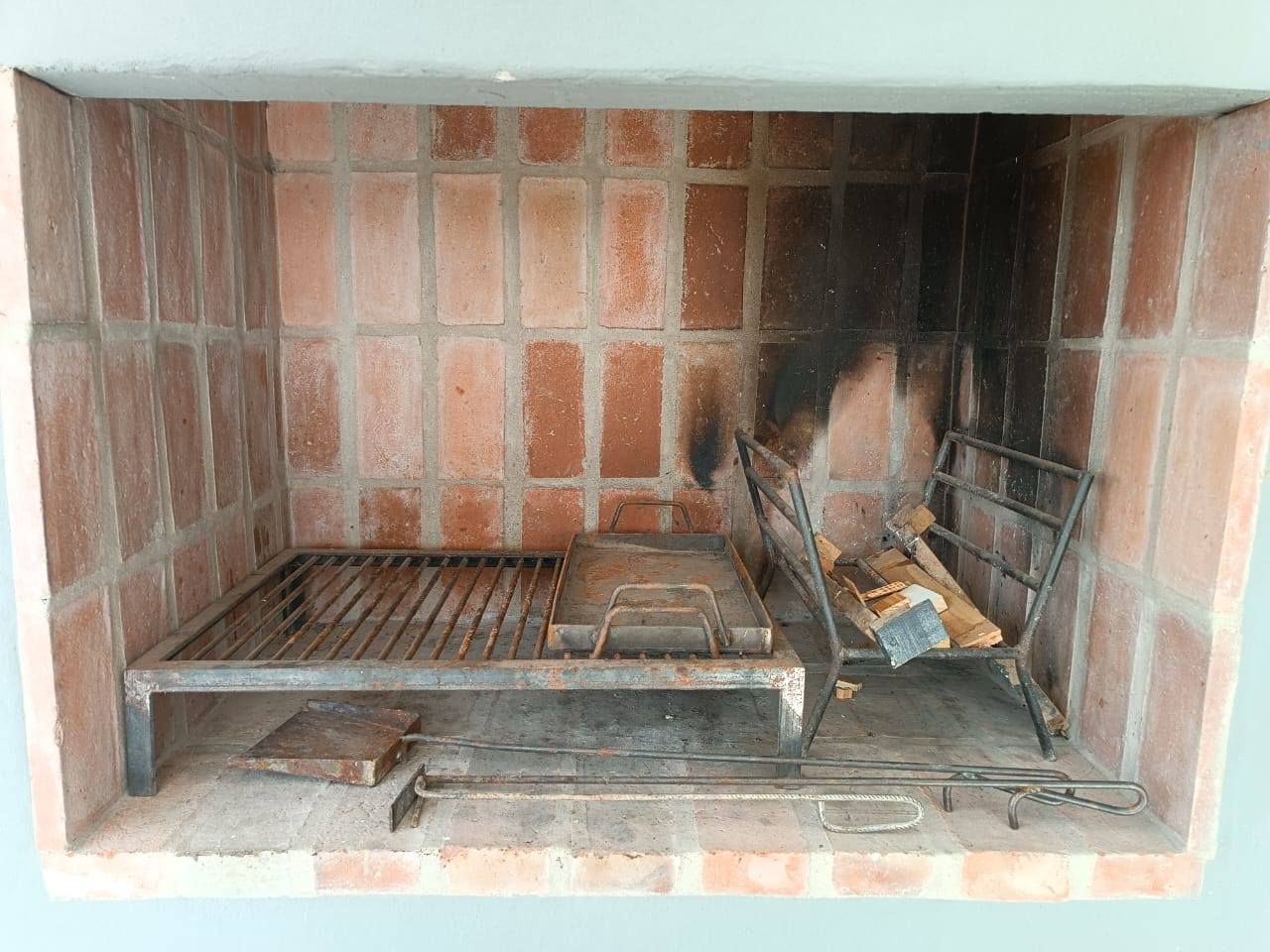 Chimenea de ladrillo con manchas de hollín, rejilla metálica y troncos cubiertos de ceniza en el interior.