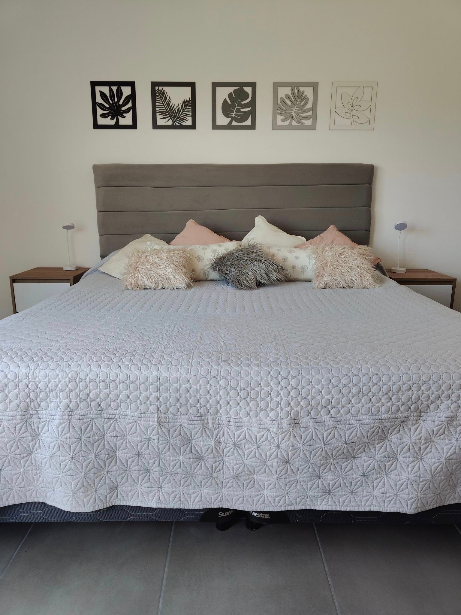 Una cama bien hecha con ropa de cama estampada, almohadas y cuadros enmarcados en la pared, en un dormitorio sencillo.