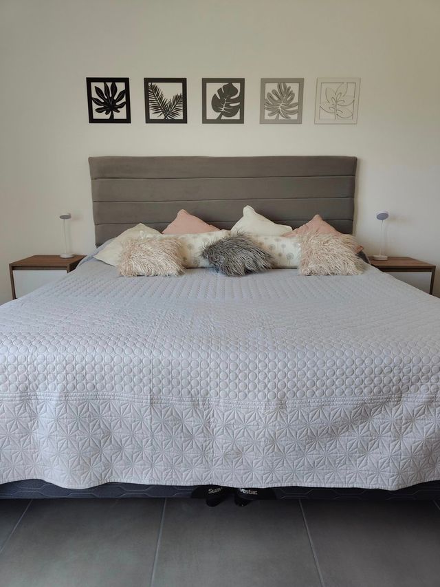 Una cama bien hecha con ropa de cama estampada, almohadas y cuadros enmarcados en la pared, en un dormitorio sencillo.