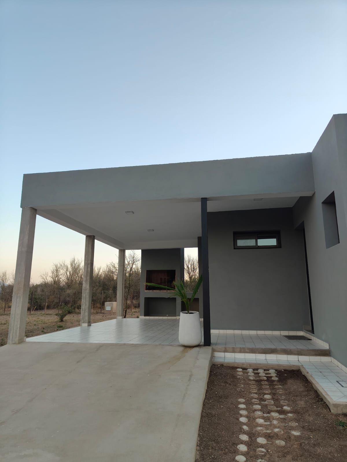 Casa moderna gris con porche, cochera cubierta y entrada de concreto al atardecer.