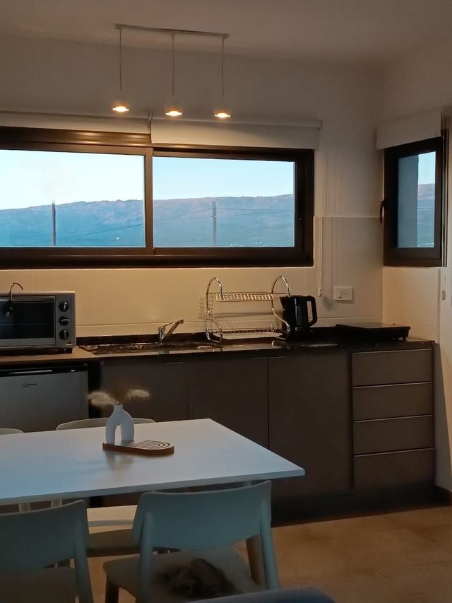 Cocina moderna con mesa blanca, armarios oscuros y un gran ventanal con vistas a las montañas.