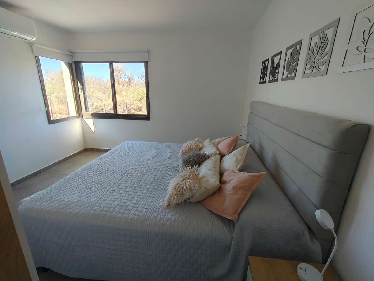 Habitación luminosa con una cama gris, animales de peluche y una ventana con vistas a los árboles.