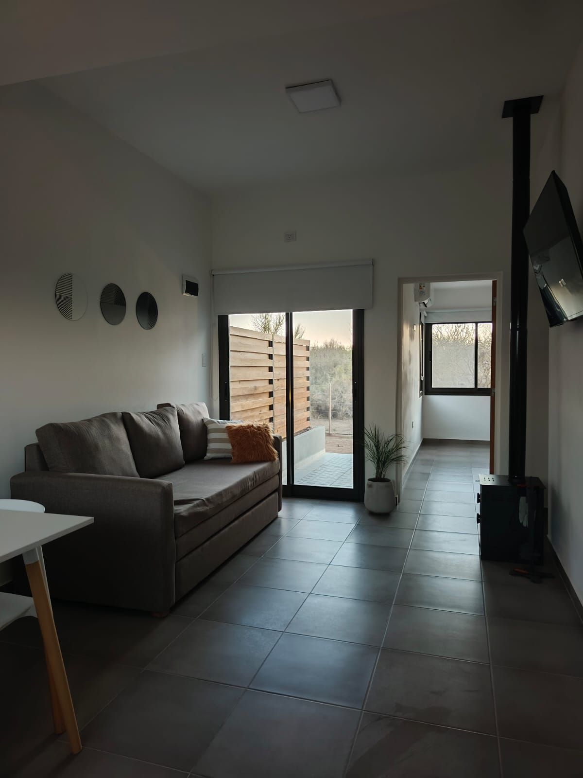 Pequeña sala de estar con sofá gris, suelo de baldosas y puertas que dan a un balcón con vistas a la ciudad.