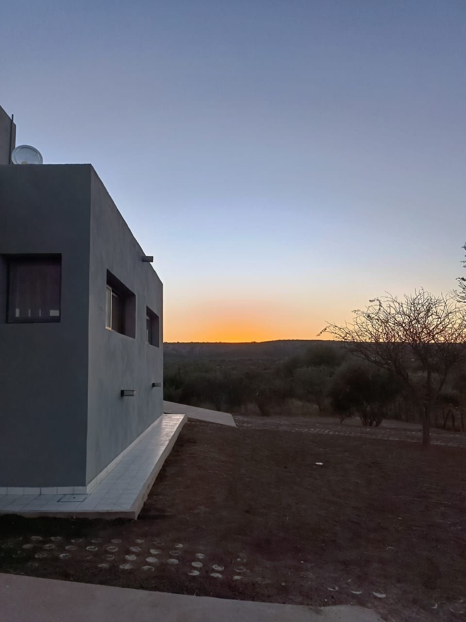 Edificio moderno de color gris al atardecer, con un horizonte anaranjado sobre un paisaje tranquilo.