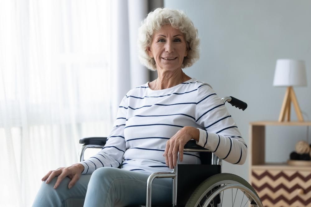 An Elderly Woman is Sitting in a Wheelchair in Front of a Window — Serenity Strides in Redbank Plains, QLD