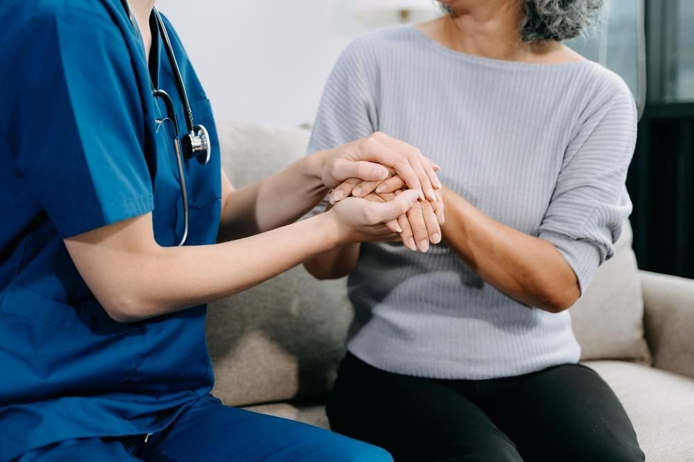 Nurse is Holding the Hand of an Elderly Woman While Sitting on a Couch — Serenity Strides in Redbank Plains, QLD