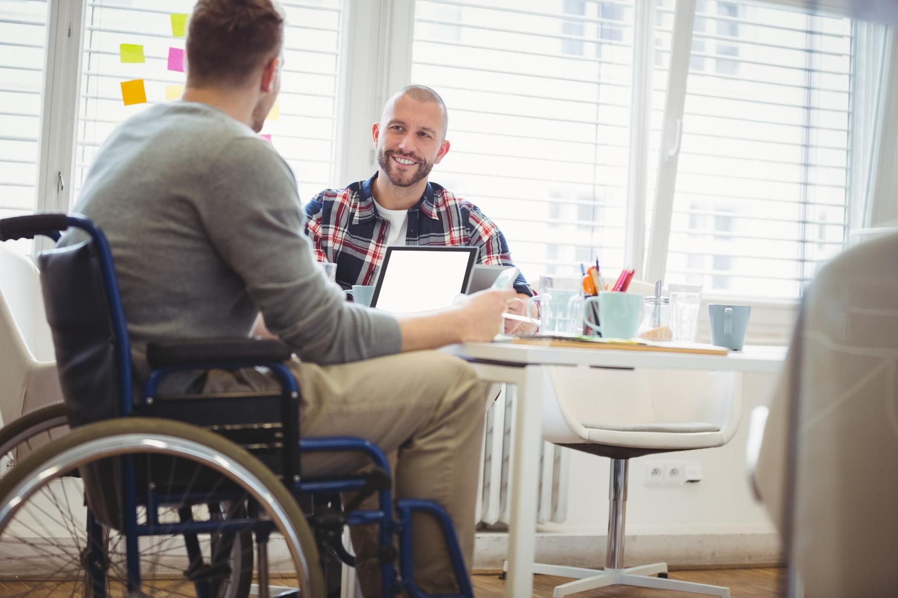 Man in a Wheelchair is Sitting at a Table Talking to Another Man — Serenity Strides in Logan, QLD