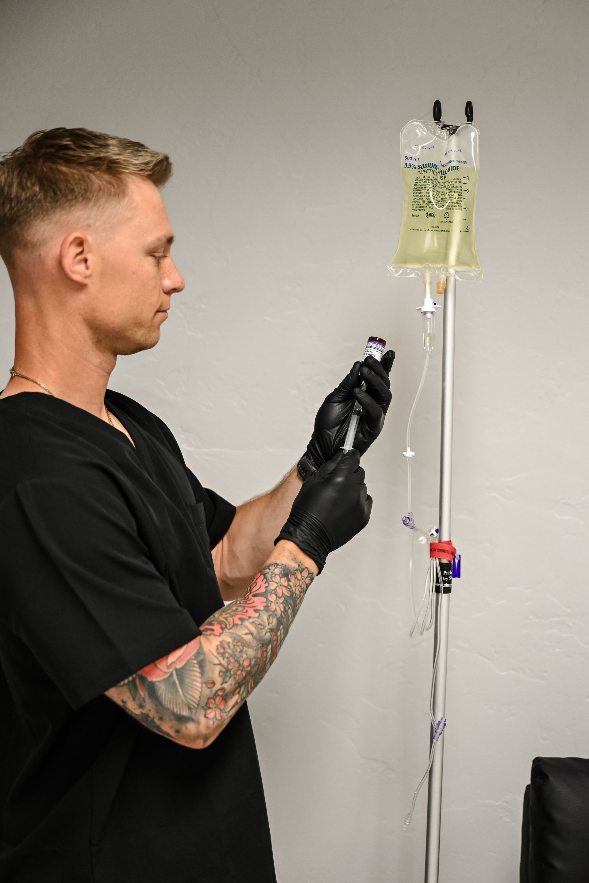 Man preparing IV bag and tubing beside a wall-mounted IV stand