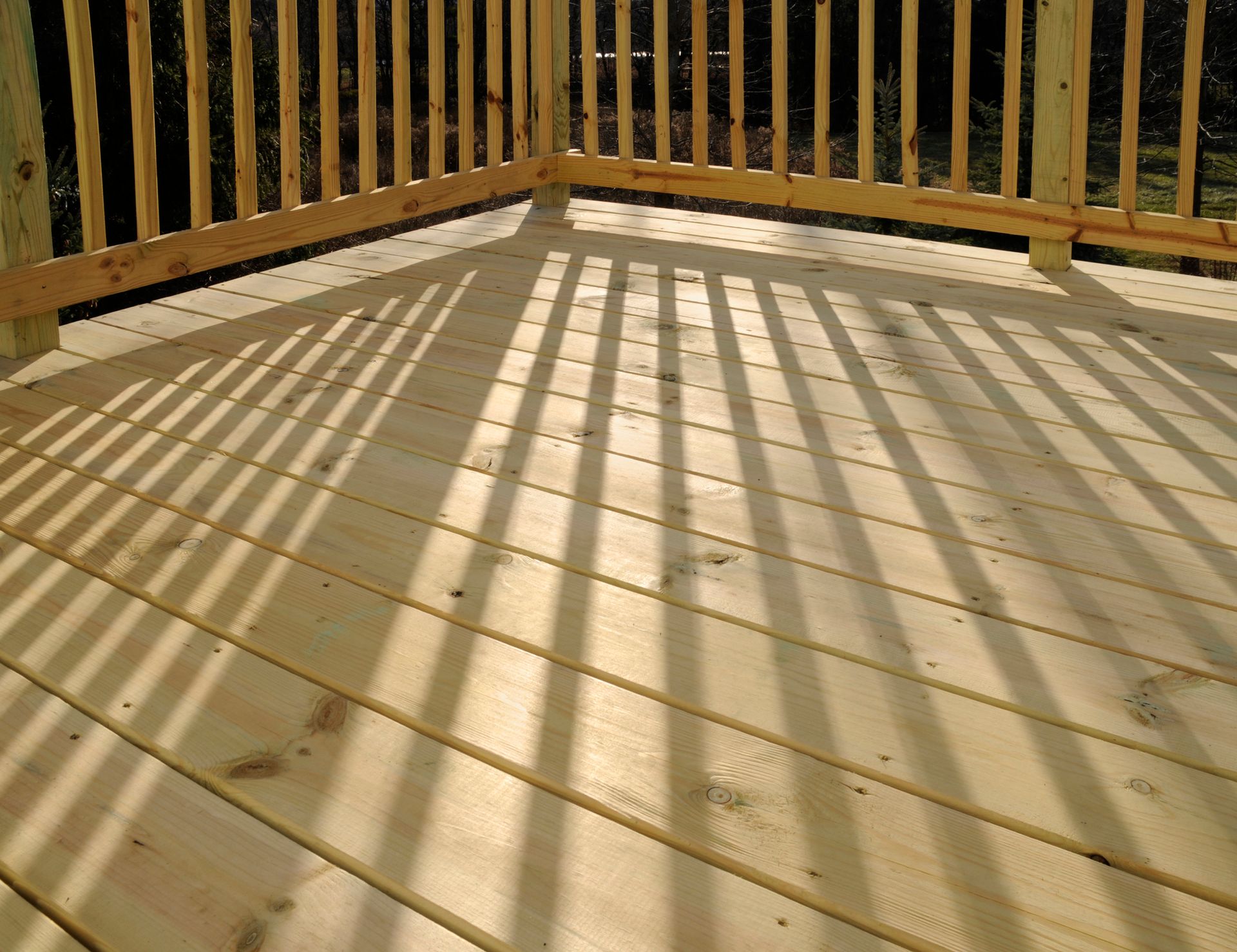 Wooden deck with railing, casting long shadows from the sunlight.