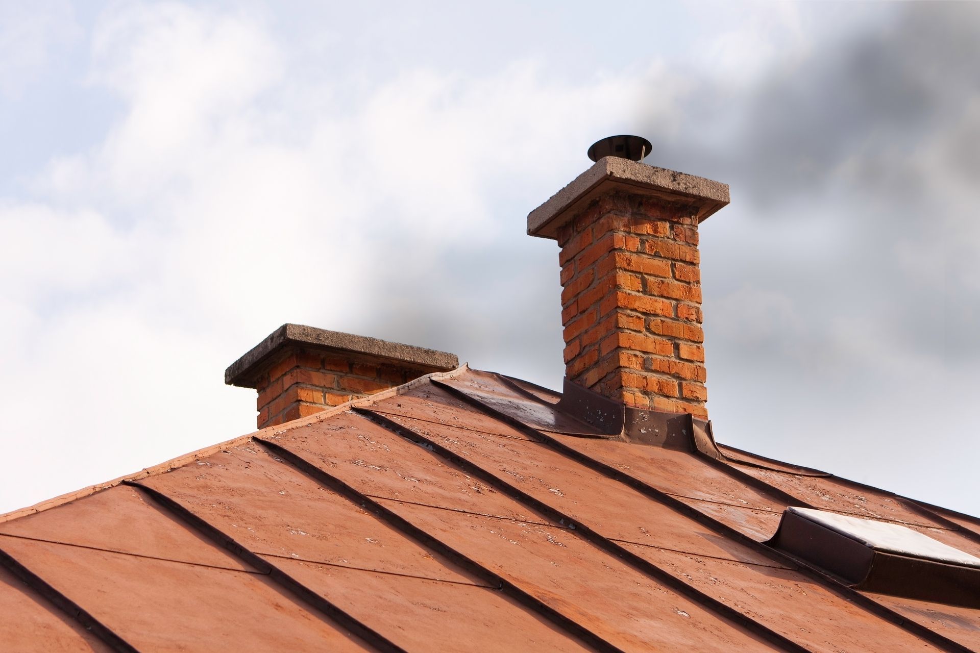 Red brick chimneys on a brown metal roof against a cloudy sky.