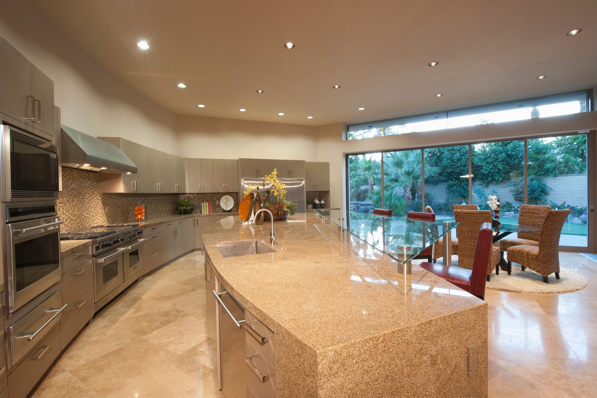 Spacious modern kitchen with large granite island, stainless steel appliances, and floor-to-ceiling windows overlooking a patio.