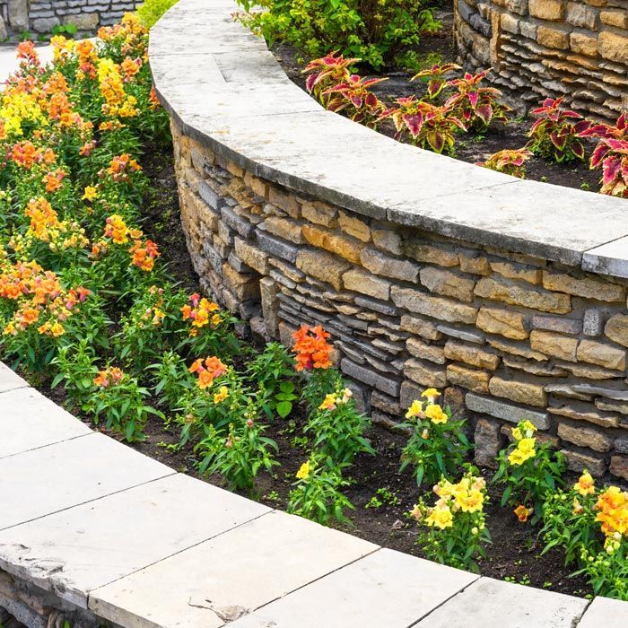 Curved stone garden wall edging a flower bed with orange and yellow blooms beside a paved path