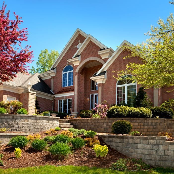 Brick suburban house with manicured landscaping, stone retaining walls, and a bright blue sky