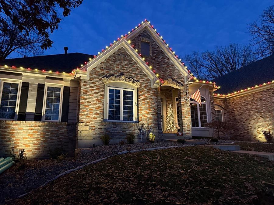Stone house exterior at dusk with warm Christmas lights along the roofline and front windows.