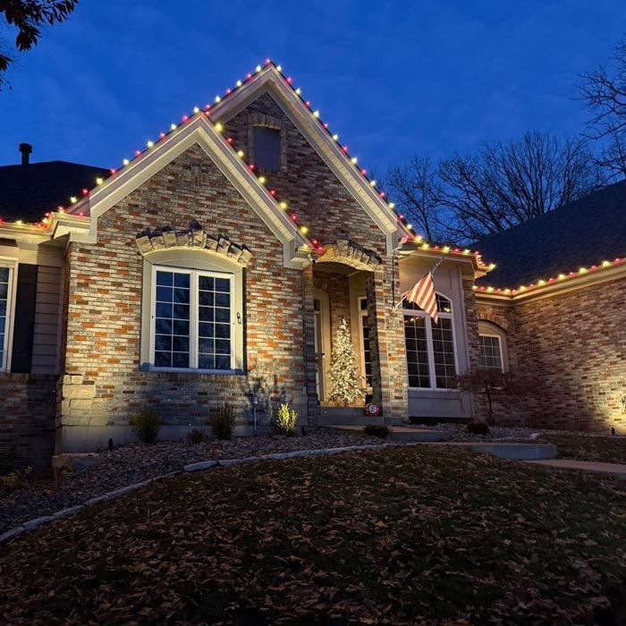 Brick house at dusk with warm holiday lights along the roofline and windows.