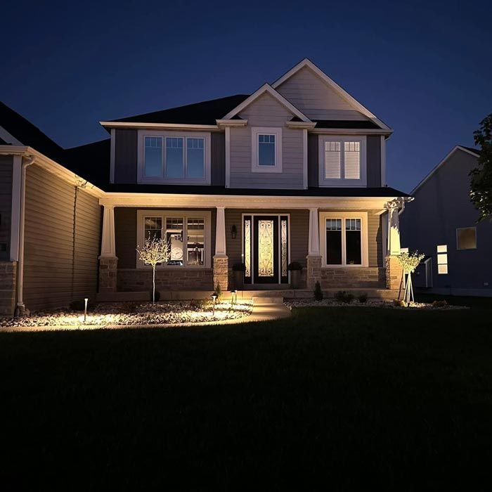 Two-story house at dusk with warm porch lights and a dark front yard