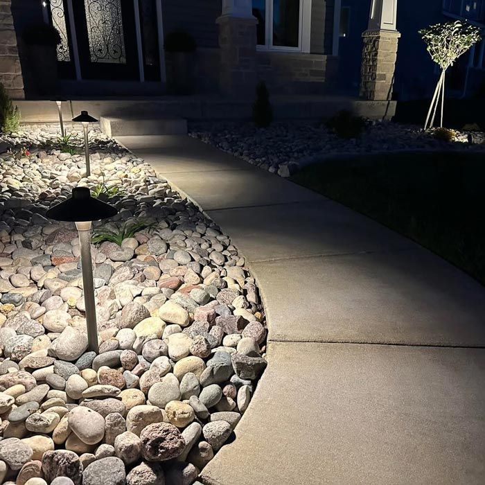 Curved concrete walkway lit by low garden lights beside a pebble landscape at night