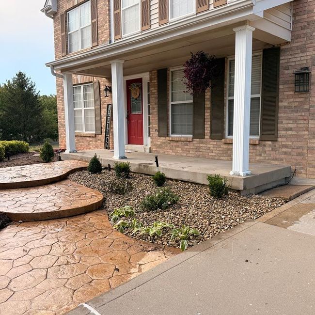 Brick house front porch with red door, white columns, and a landscaped stone walkway