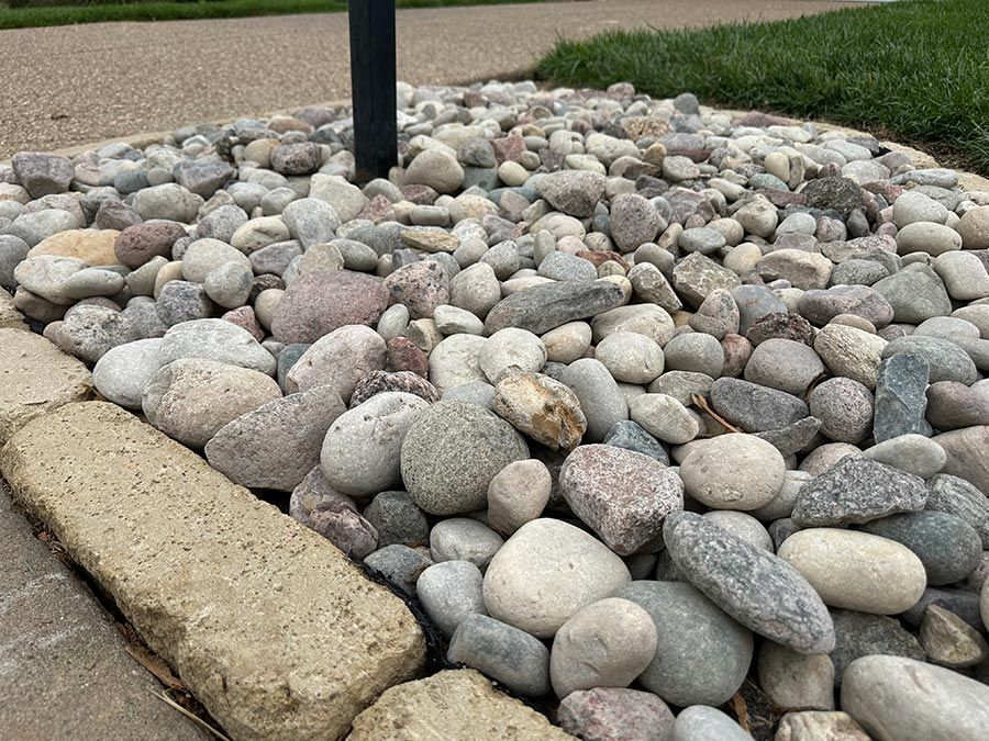 Pebble-filled landscape bed bordered by stone edging with a black post in the center