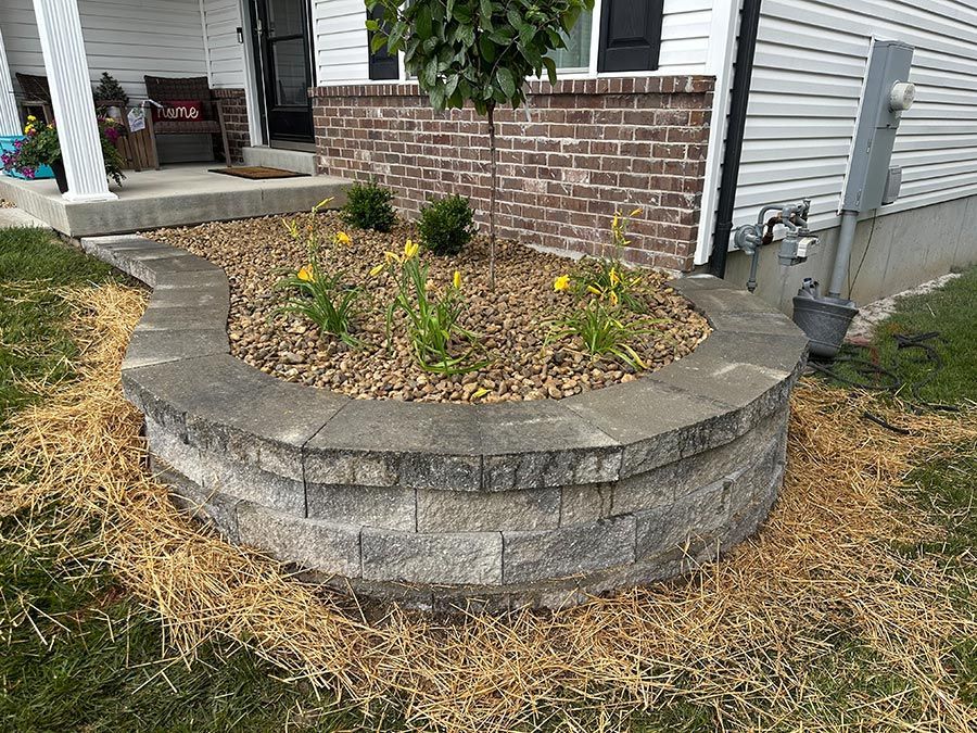 Brick raised flower bed with small yellow flowers beside a house porch and siding