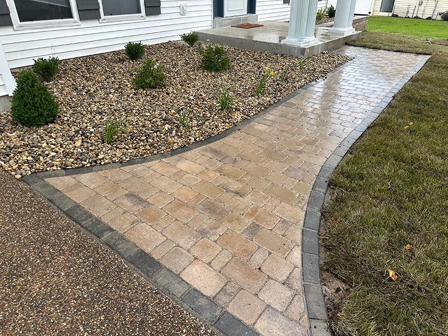 Brick walkway with dark edging leading to a house porch beside a gravel garden bed