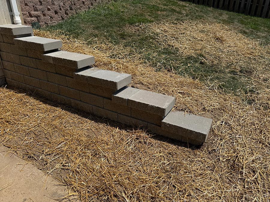 Stacked gray cinder blocks forming a stepped retaining wall beside a dry, mulched yard.