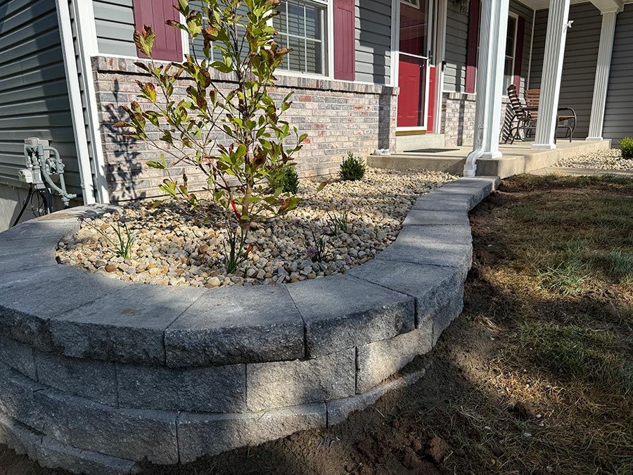 Stone retaining wall around a small landscaped front yard by a house entrance