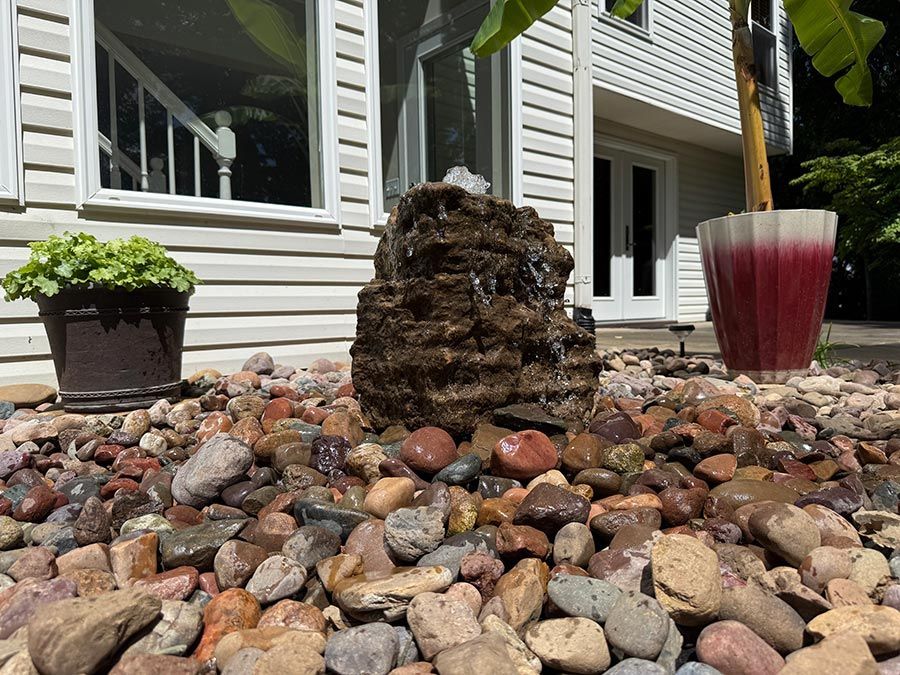 Rock garden with river stones, a potted plant, and a red planter outside a house.
