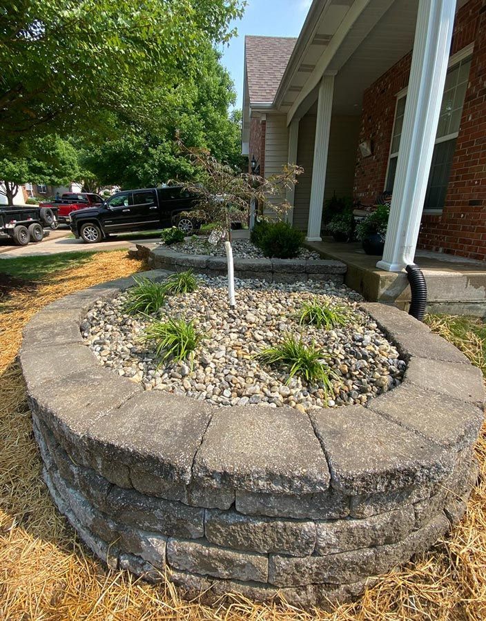 Stone planter with a small tree and mulch beside a brick house porch