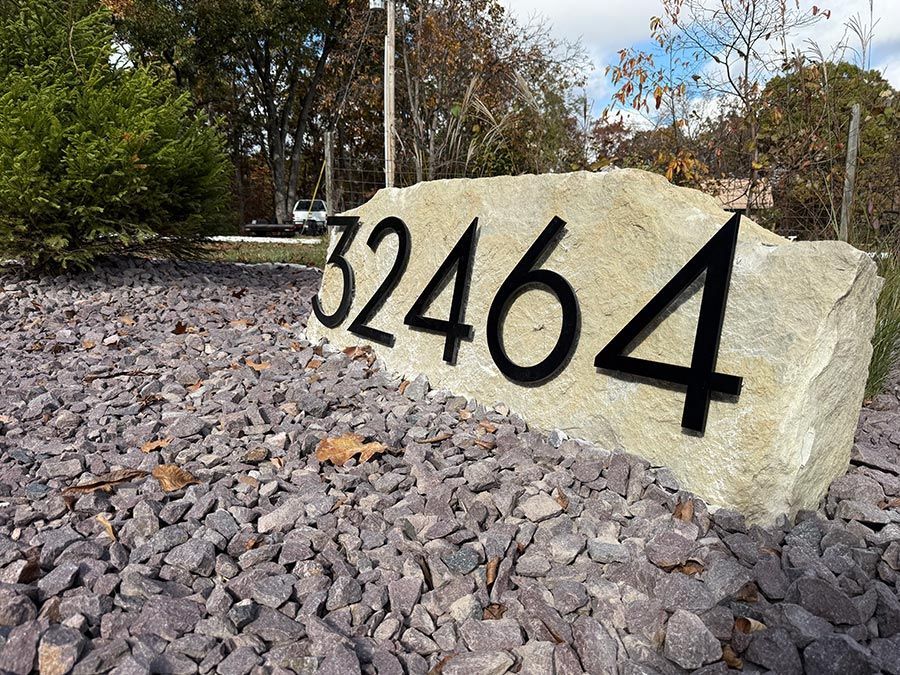 Stone address marker reading 32464 beside a gravel landscape with trees in the background