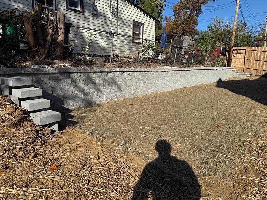 Backyard with a gravel slope, retaining wall, small concrete steps, and house beside a wooden fence