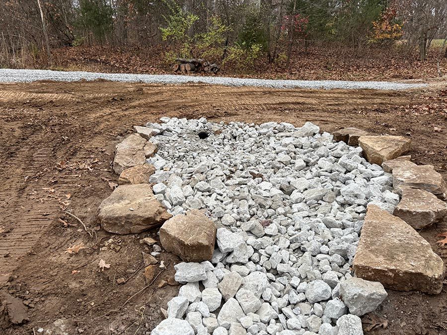 Rock-filled drainage area bordered by large stones in a muddy outdoor construction site.