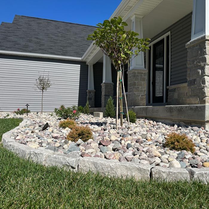 Front yard landscaping with white rocks, small tree, and stone edging beside a house and garage