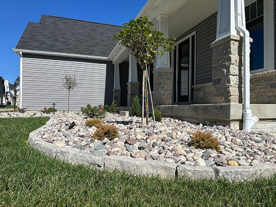 Suburban house front yard with rock landscaping, small trees, and a grassy lawn