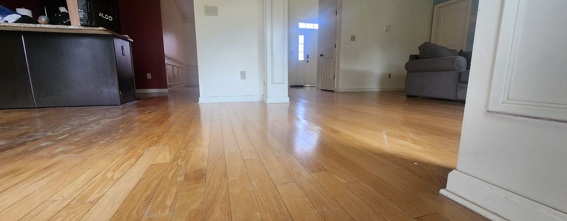 Wooden floor in a room, with sunlight shining through a distant doorway.  A gray armchair is visible.