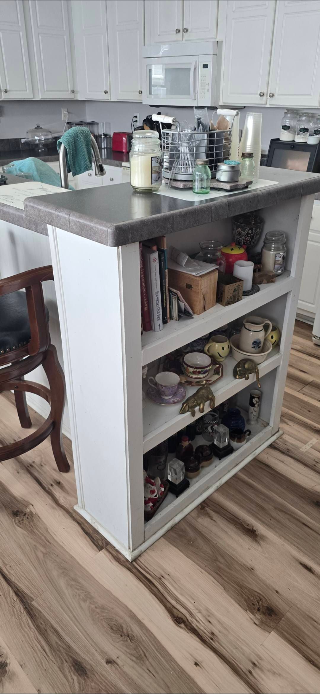 White kitchen island with open shelves holding various items. Countertop, wood flooring, and cabinetry visible.