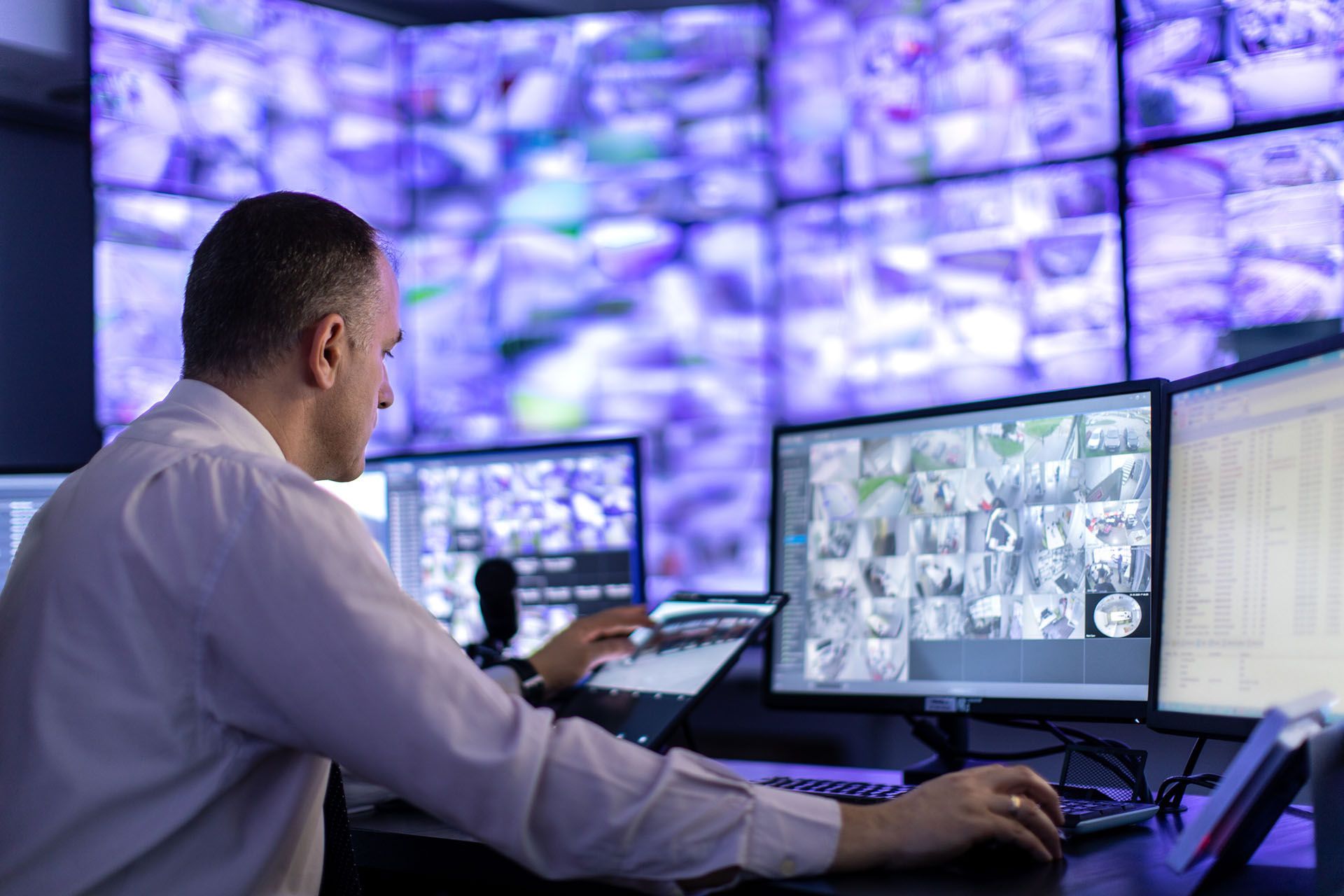 A man is sitting at a desk in front of a bunch of computer monitors A man is sitting at a desk in front of a bunch of computer monitors