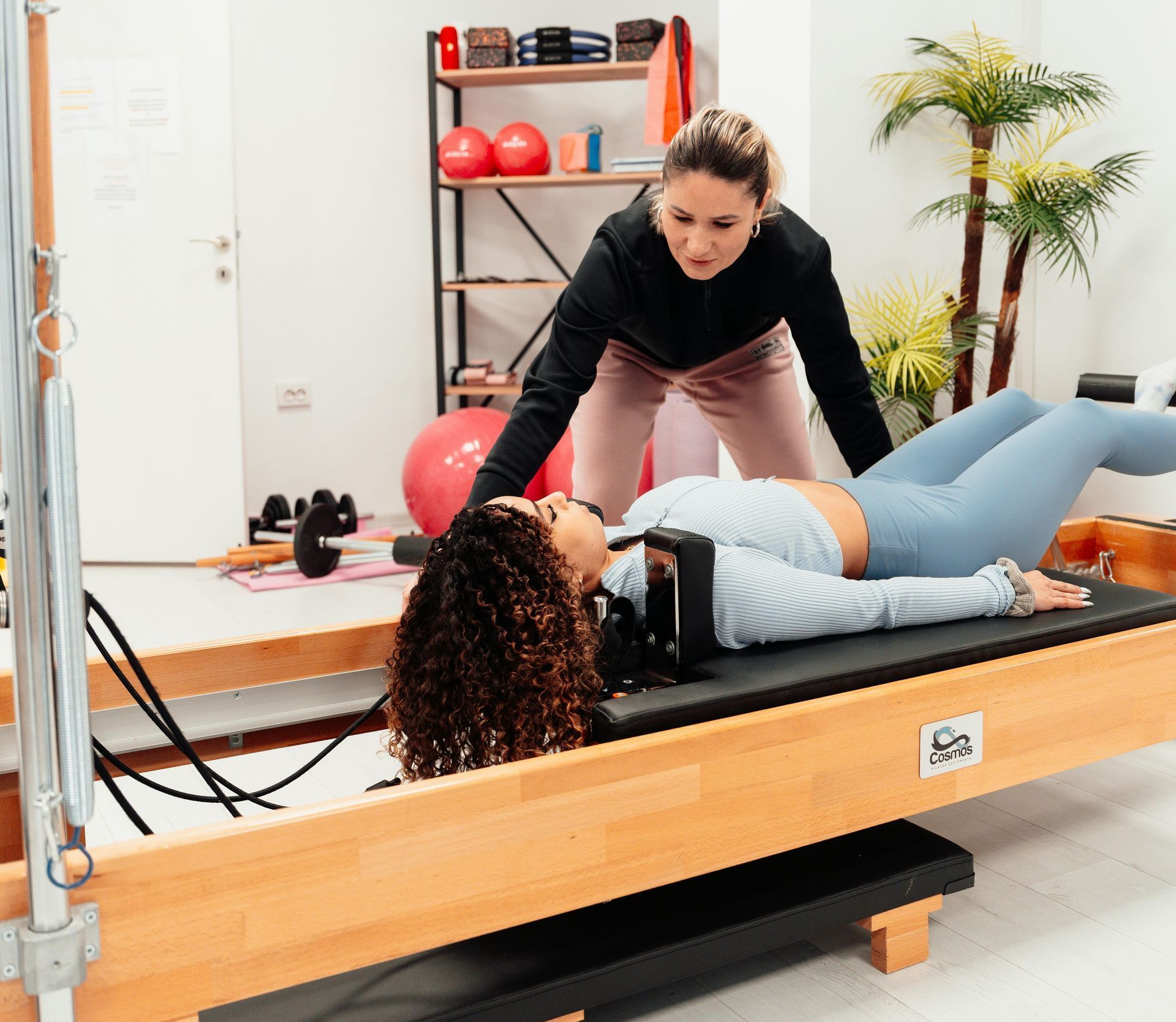 A woman is laying on a pilates machine while another woman helps her.