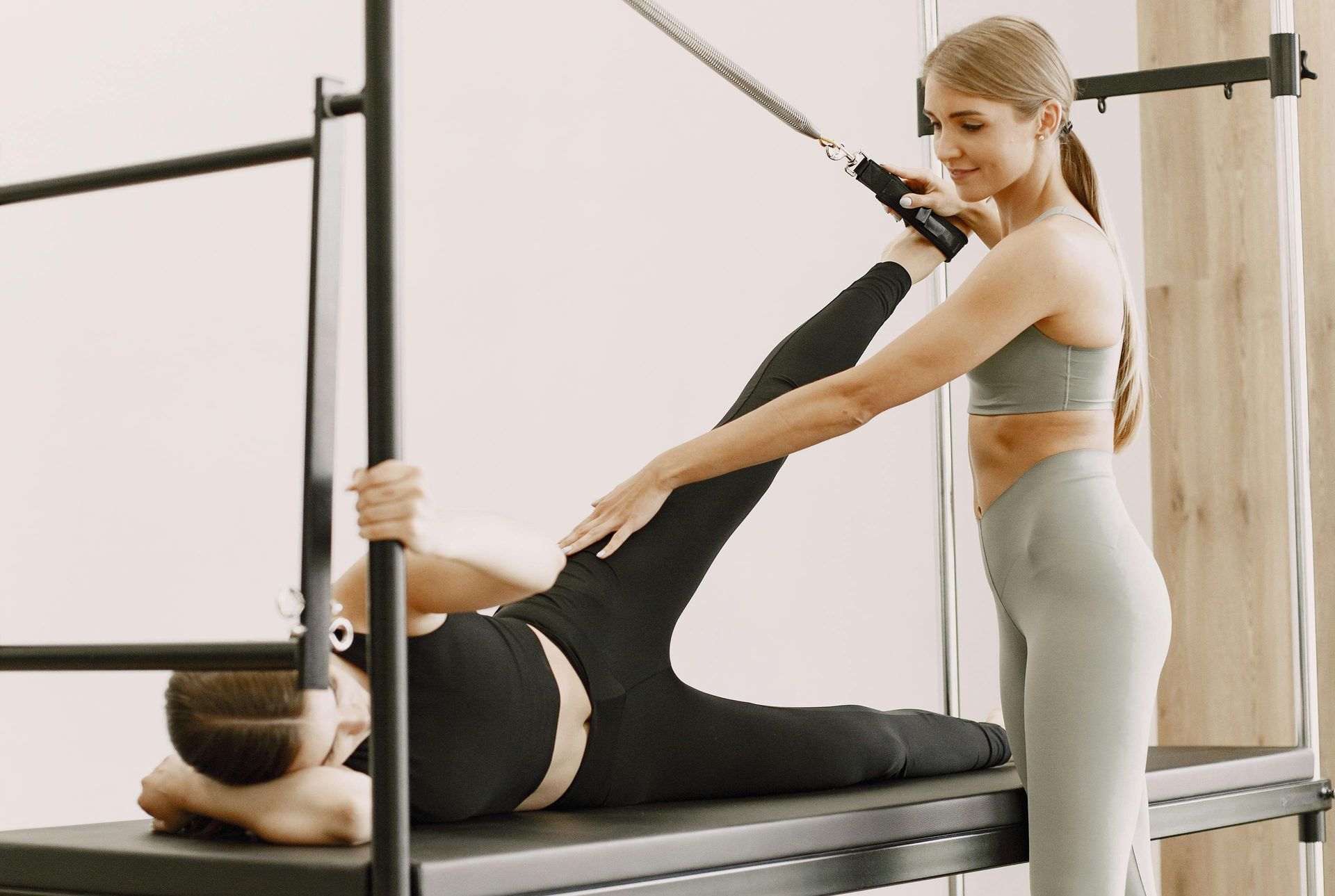 A woman is helping another woman do pilates on a pilates machine.
