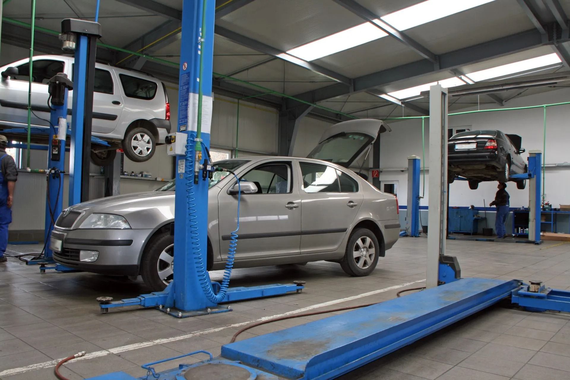 Officina meccanica con auto sollevate su piattaforme elevatrici blu all'interno di un garage.