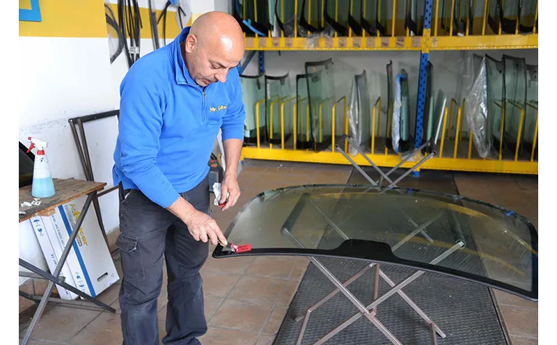 Un uomo con una camicia blu ispeziona un grande pannello di vetro in un'officina