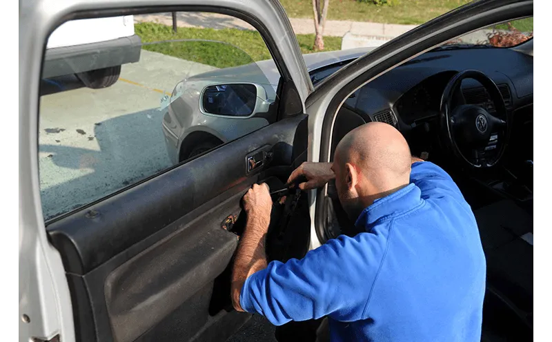 Uomo con camicia blu che rimuove il pannello interno della portiera di un'auto bianca