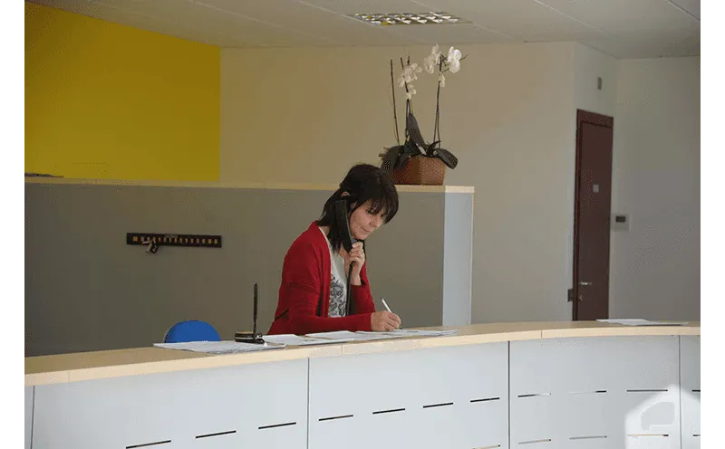 Persona che scrive a una scrivania in un ufficio moderno con parete gialla e armadietti bianchi.