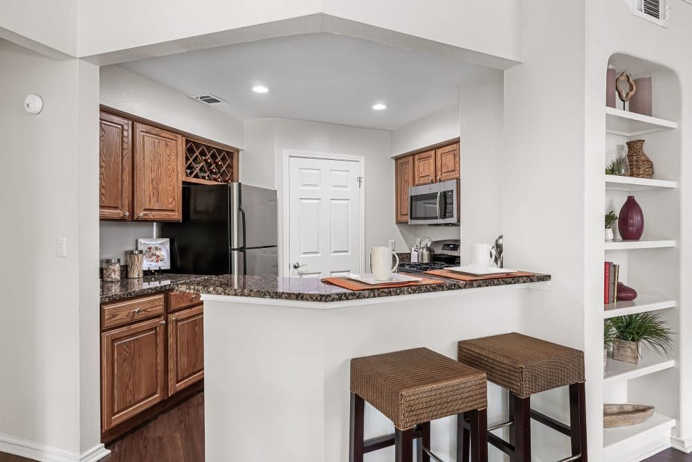 A kitchen with wooden cabinets, granite counter tops, a refrigerator, microwave, and stools at Marquis at Caprock Canyon in Austin, TX.