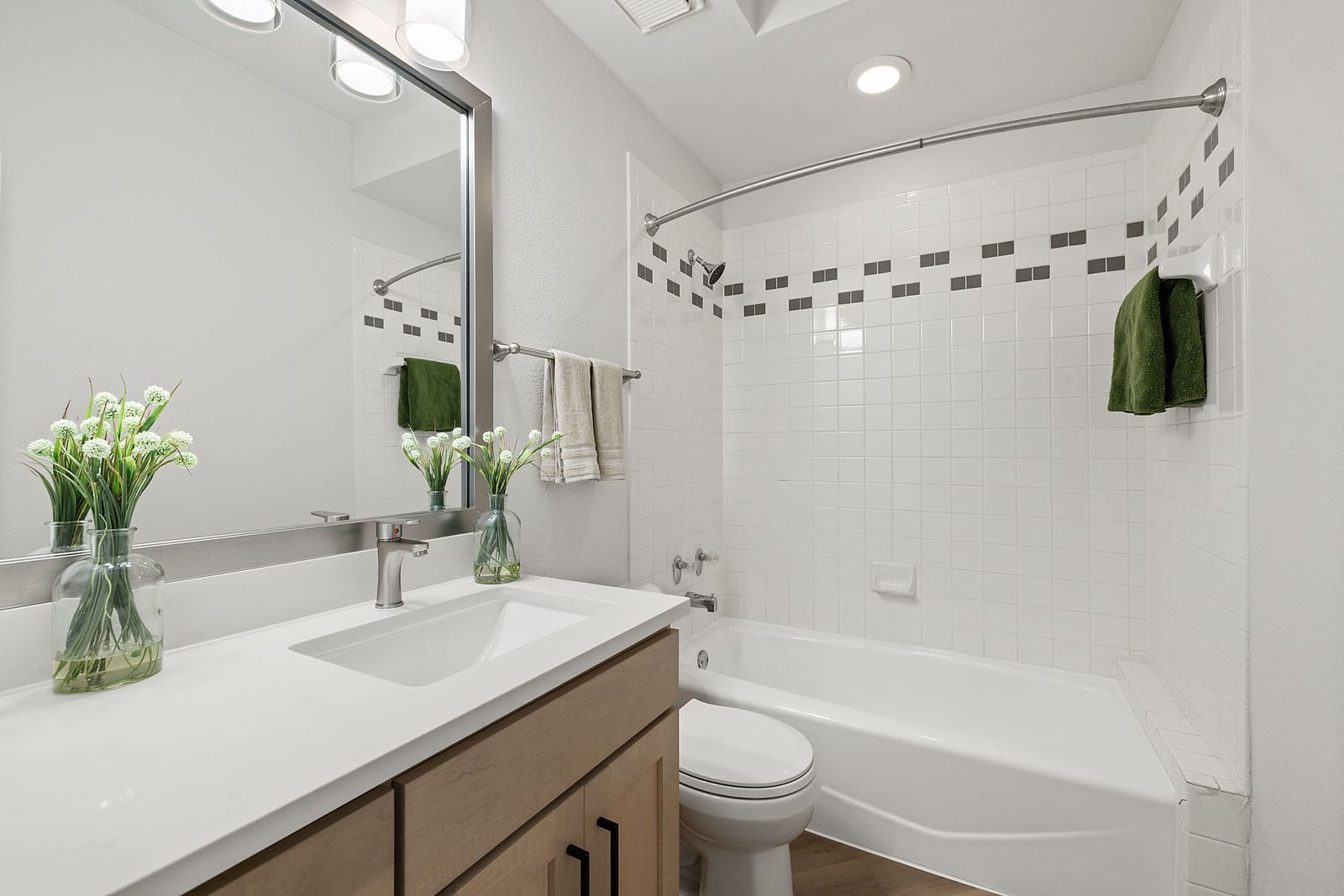 Bright white bathroom with vanity sink, large mirror, bathtub, and green towels at Marquis at Caprock Canyon in Austin, TX.
