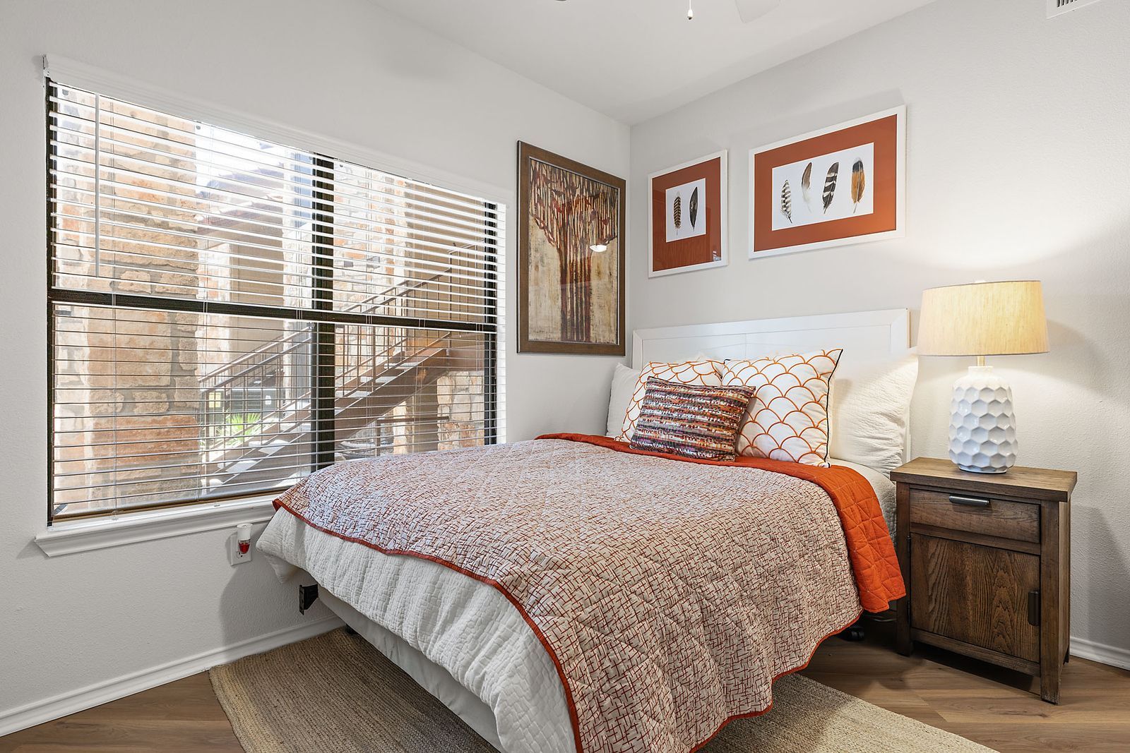 Cozy bedroom with a bed, bedside lamp, framed art, and a large window with blinds at Marquis at Caprock Canyon in Austin, TX.