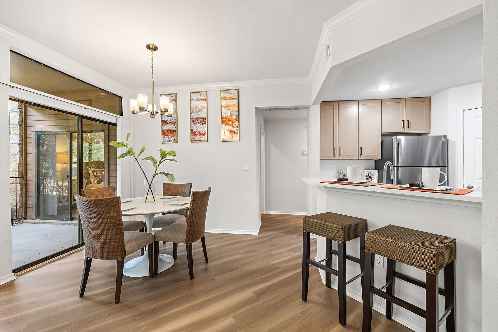 Bright dining and kitchen area with wicker chairs, bar stools, wood floors, and sliding glass doors at Marquis at Caprock Canyon in Austin, TX.