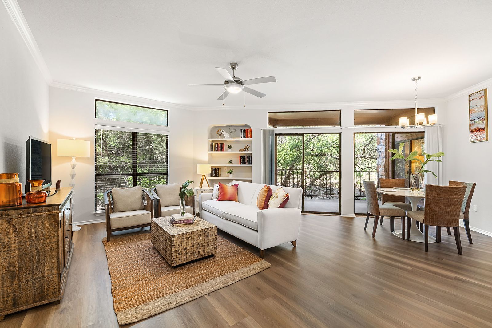 Bright open living and dining room with white sofa, wood floors, large windows, and patio doors at Marquis at Caprock Canyon in Austin, TX.