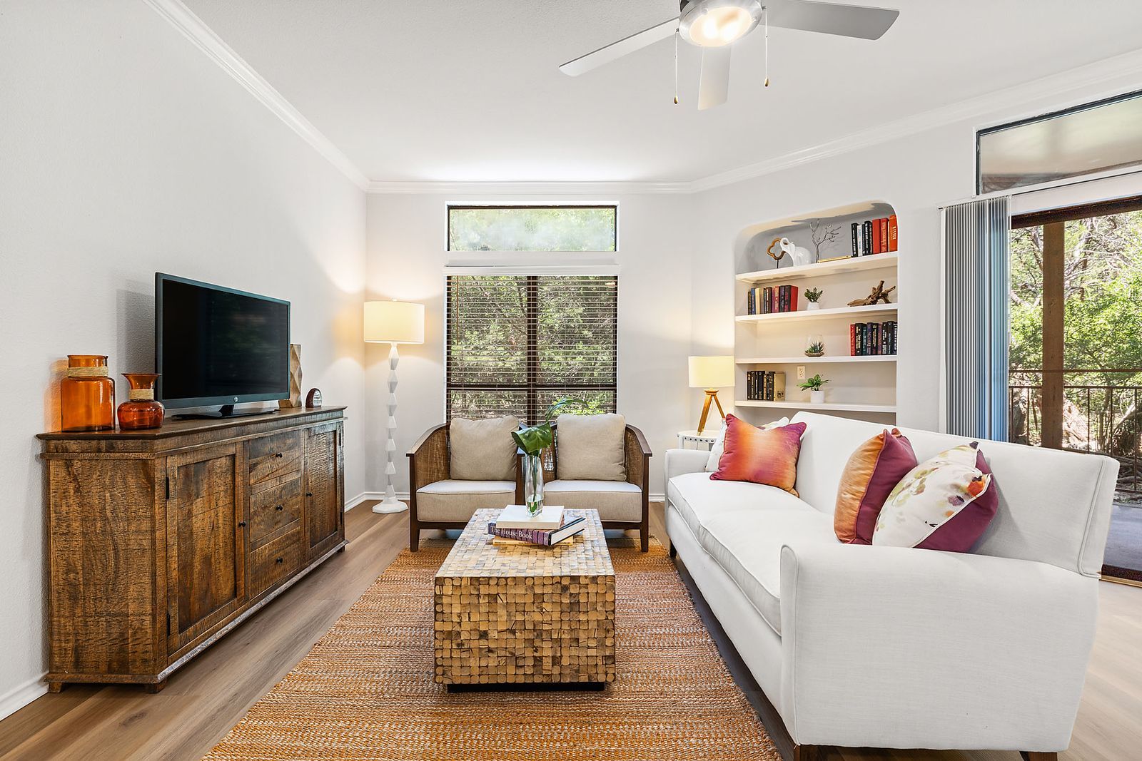 Bright living room with white sofa, wicker coffee table, TV console, and large windows at Marquis at Caprock Canyon in Austin, TX.