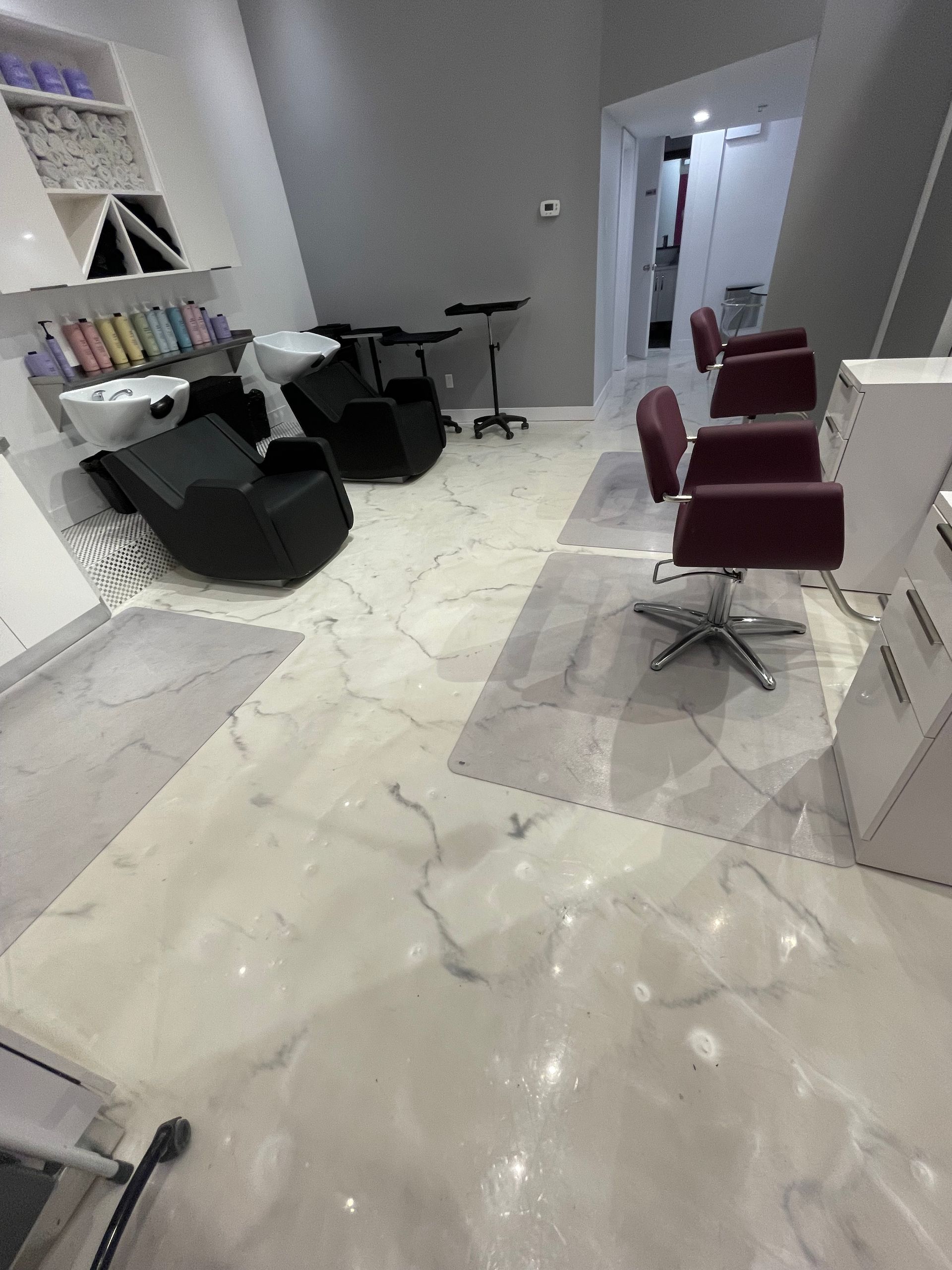 Salon interior with black and red chairs, white marble floors, and grey walls.